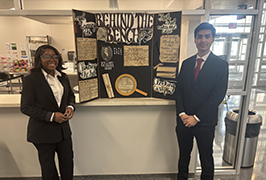  Two students stand wearing business dress in front of a trifold.